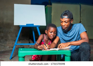 A Young African Brother Or Father Helping Sister Or Daughter Learn - Concept On Black Millennials Studying Or Reading In The House During Covid-19 Pandemic Quarantine In Africa, Girl Child Education 