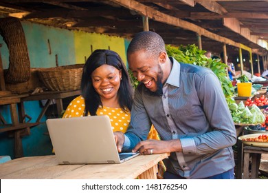 Young African Business Agent And A Local Market Woman Laughing While Viewing Something On A Laptop