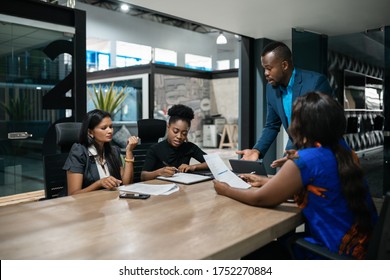 Young African businessman talking with a diverse team of colleagues during a meeting around a table in an office boardroom