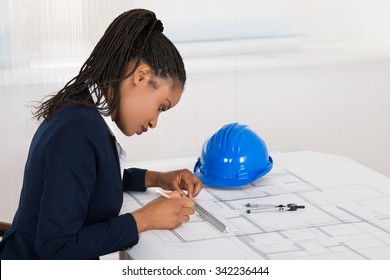 Young African Businesswoman Drawing Blueprint At Office Desk - Powered by Shutterstock