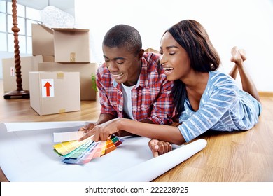 Young African Couple Having Fun Deciding On Paint Colour Swatch For New Home Apartment