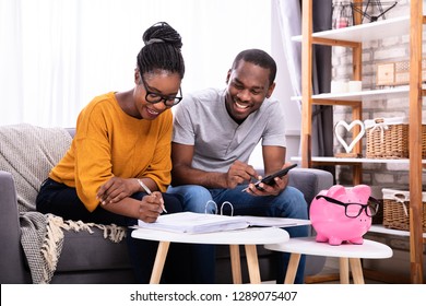 Young African Couple Sitting On Sofa Calculating Invoice