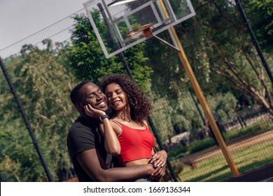 Young African Descent Couple Standing On Basketball Court Outdoors Hugging Woman Touching Man's Face Tender Smiling Happy