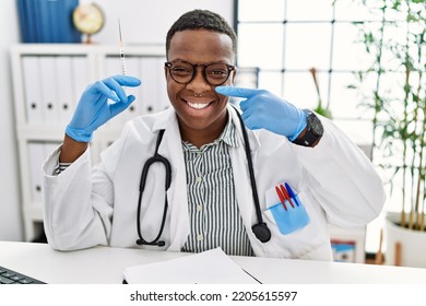 Young African Doctor Man Holding Syringe At The Hospital Pointing With Hand Finger To Face And Nose, Smiling Cheerful. Beauty Concept 