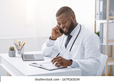 Young African Doctor Talking To Patient On Phone While Working In Modern Clinic, High Quality Service Concept