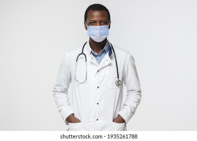 Young African Doctor Wearing Surgical Mask Is Ready To Help Patients With Coronavirus Or Covid Virus, Isolated On Gray Background 