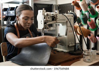 Young African female artisan sewing leather in her workshop