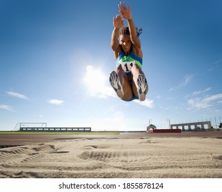 Young African female athlete mid-air during long jump at an athletics event on a bright, sunny day