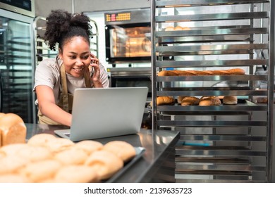 Young  African female Business owner in apron using laptop and talking to clients on the phone by workplace.Organization of Work in the Field of Delivery. - Powered by Shutterstock