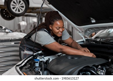 Young african female car repair worker check the oil level in car engine, side view. Smiling black mechanic checking and maintenance car engine or vehicle with herrself. Copy space