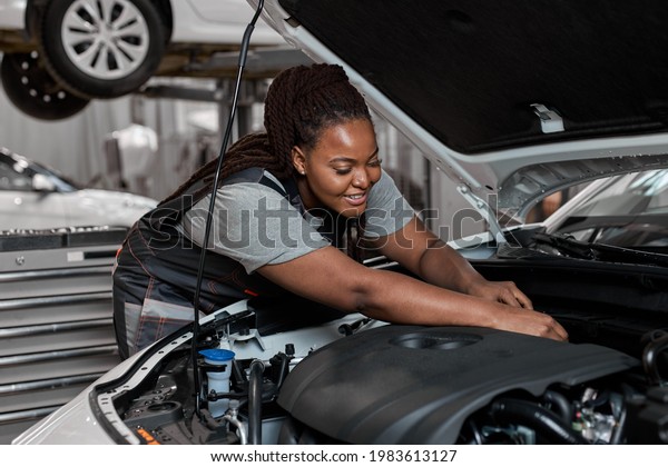 Young african\
female car repair worker check the oil level in car engine, side\
view. Smiling black mechanic checking and maintenance car engine or\
vehicle with herrself. Copy\
space