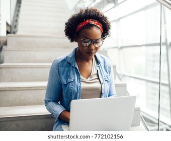 Young African female college student working on a laptop on some stairs on campus preparing for an exam - Powered by Shutterstock