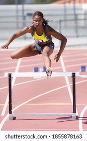 Young African female runner jumping over a hurdle at an athletics event out at the track on a bright, sunny day - Shutterstock ID 1855878163