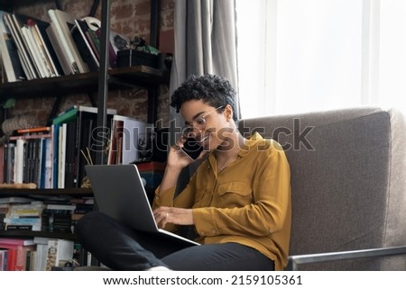 Young African female telemarketer talks to client by cellphone filling order form using laptop, solve business by phonecall. Mobile operator, modern tech usage, remote communication, telework concept