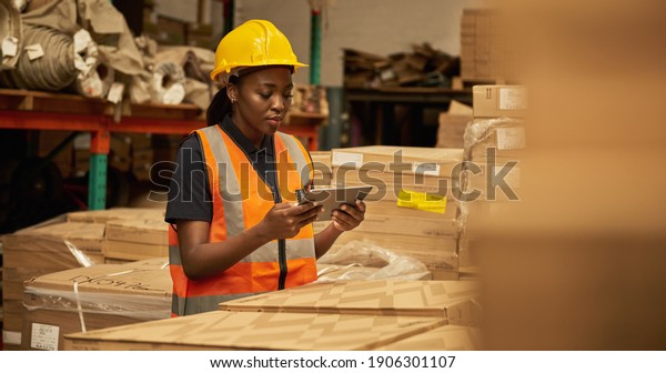 Young African female warehouse worker\
working on a digital table during an iventory\
check