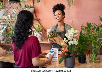 Young african florist holding bouquet of fresh flower while customer making digital payment with smartphone while scanning QR code. Black saleswoman giving a bunch of flower to customer at botany shop - Powered by Shutterstock