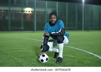 Young African footballer with soccer ball sitting on squats while having rest on football field after training on stadium - Powered by Shutterstock