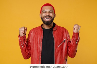 Young african fun man 20s with funky trendy pink hairdo in stylish red leather jacket black t-shirt do winner gesture clench fist celebrating isolated on yellow orange color background studio portrait - Shutterstock ID 2170619647