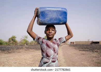 Young African girl carrying a heavy water container on her head, symbolising traditional roles of women in society blocking access to education, equal rights and independence