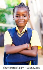 An Young African Girl In Her Blue And Yellow School Uniform And Backpack, Standing Proud With Her Arms Crossed.