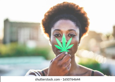 Young african girl holding marijuana leaf - Cannabis medicine, healthy lifestyle and ecology concept - Focus on leaf