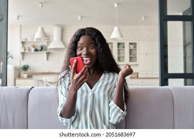 Young African girl at home reading message on mobile phone on unexpected news, happy client winning online shopping promo, gets prize in social media giveaway. Good luck big win concept.