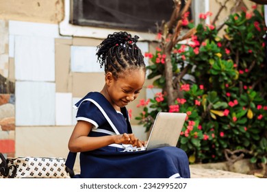 young African girl immersed in her school work, using a laptop computer on a bench - Powered by Shutterstock