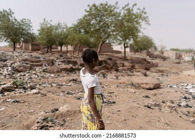 Young african girl standing with her back to the camera pointing to the desolate landscape of her homeland characterized by climate change, desertification and waste pollution