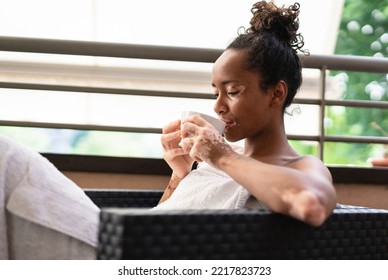 Young african girl with vitiligo relaxing and drinking tea in robes during wellness day on the rooftop of spa - Shutterstock ID 2217823723