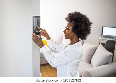 Young African Girl Woman Lady Adjusting Remote Climate Control Panel Settings Wall Touch Screen Set Heating Conditioning Switch On Security System Energy Saving Mode, Black Lady Use Smart Home Concept