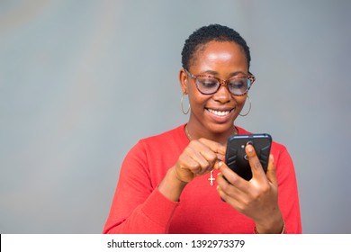young african lady with short hair cut and wearing glasses smiling and pushing a button on her smartphone screen