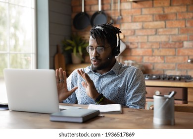 Young african male in headphones engaged in distant learning answer on teacher question at virtual class held by video conference. Millennial black man capable expert assist client online using laptop