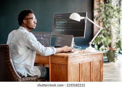 Young african male programmer writing program code sitting at the workplace with three monitors in the office. Image focused on the screen - Shutterstock ID 1233182212