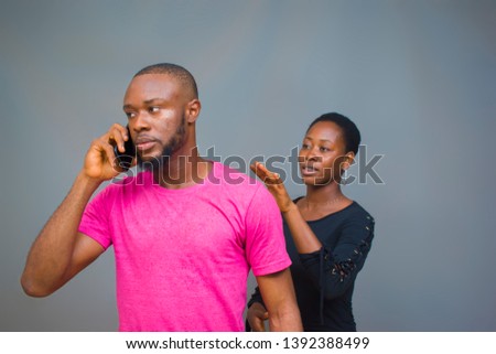 a young African man angrily making a call with a lady behind trying to talk to him