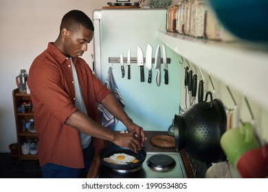 Young African Man Cracking Eggs Into A Frying Pan