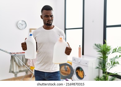 Young African Man Doing Laundry Holding Detergent Bottles Skeptic And Nervous, Frowning Upset Because Of Problem. Negative Person. 