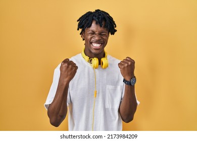 Young african man with dreadlocks standing over yellow background very happy and excited doing winner gesture with arms raised, smiling and screaming for success. celebration concept. 