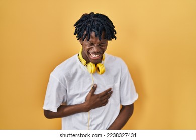 Young african man with dreadlocks standing over yellow background smiling and laughing hard out loud because funny crazy joke with hands on body.  - Powered by Shutterstock