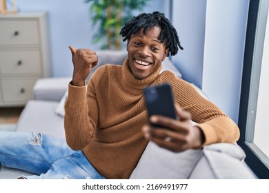 Young african man with dreadlocks using smartphone doing video call pointing thumb up to the side smiling happy with open mouth  - Powered by Shutterstock