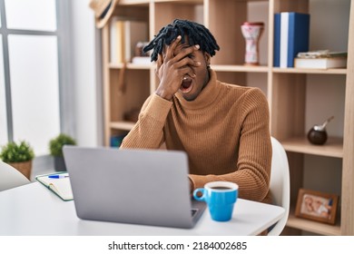 Young African Man With Dreadlocks Working Using Computer Laptop Peeking In Shock Covering Face And Eyes With Hand, Looking Through Fingers With Embarrassed Expression. 