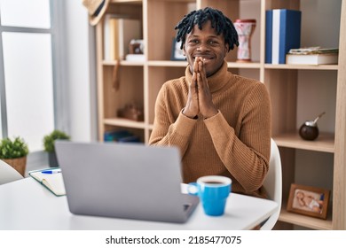 Young African Man With Dreadlocks Working Using Computer Laptop Praying With Hands Together Asking For Forgiveness Smiling Confident. 