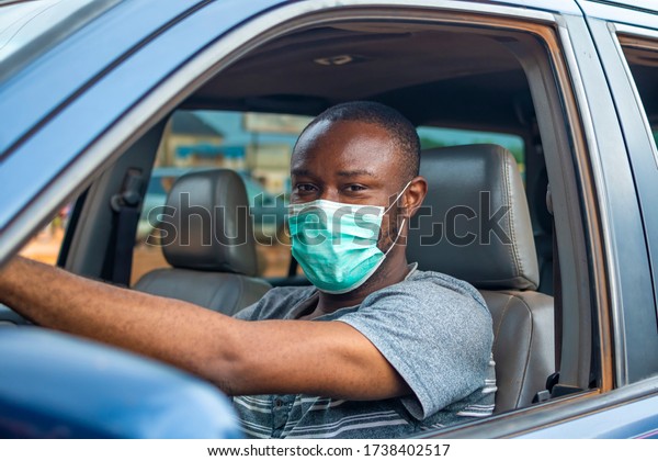 young\
african man driving a car wearing a face\
mask
