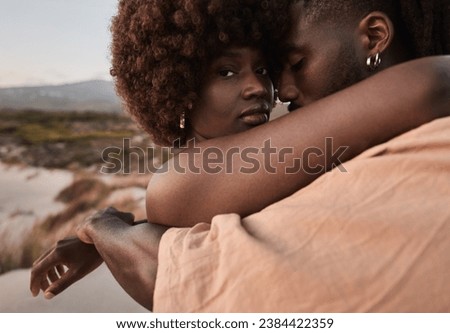 Young African man embracing girlfriend with Afro hair and tattoo standing against mountain on seacoast during romantic vacation