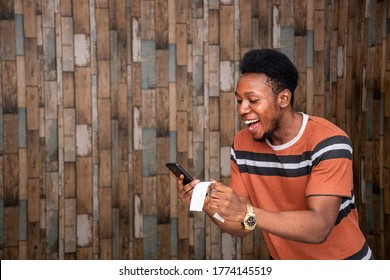 A Young African Man Feeling Happy And Excited Holding His Phone And A Slip, Celebrating