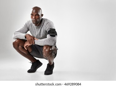 Young African Man With Headphones Crouching With Copy Space. Black Male Model Listening To Music On Grey Background .