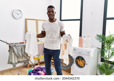 Young African Man Holding Clean White T Shirt And T Shirt With Dirty Stain Smiling And Laughing Hard Out Loud Because Funny Crazy Joke. 