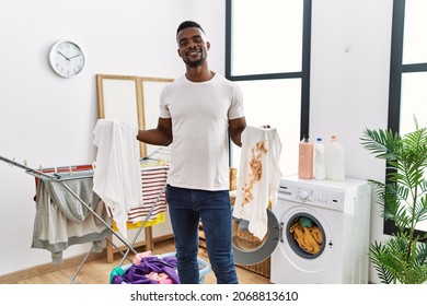 Young African Man Holding Clean White T Shirt And T Shirt With Dirty Stain Smiling With A Happy And Cool Smile On Face. Showing Teeth. 