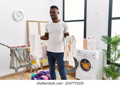 Young African Man Holding Clean White T Shirt And T Shirt With Dirty Stain Winking Looking At The Camera With Sexy Expression, Cheerful And Happy Face. 