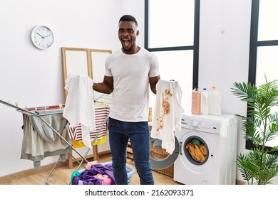 Young African Man Holding Clean White T Shirt And T Shirt With Dirty Stain Celebrating Crazy And Amazed For Success With Open Eyes Screaming Excited. 