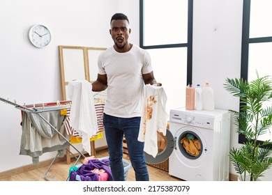 Young African Man Holding Clean White T Shirt And T Shirt With Dirty Stain Afraid And Shocked With Surprise And Amazed Expression, Fear And Excited Face. 